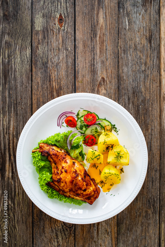 Cooked rabbit thighs with potatoes and fresh vegetable salad on wooden table

