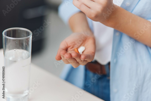 Woman holding a pill in front of a glass of water  healthcare and medicine concept