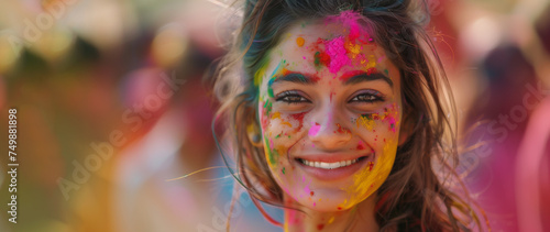 Holi festival. Smiling Indian young woman with colourful powder on her face. Widescreen banner, copy space.