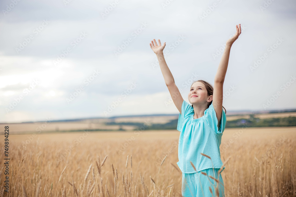 Teenage girl in blue dress standing in field against sky background with hands raised up. Teenage girl in blue dress standing in field against sky background with hands raised up.