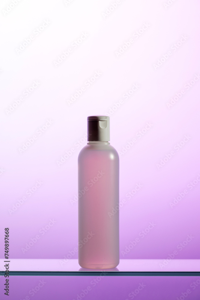 A plastic bottle with liquid cosmetics and tonic stands on a glass shelf A plastic bottle with liquid cosmetics and tonic stands on a glass shelf