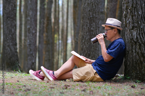 Man sitting under a tree in the pine forest, drinking cold drink from a tumbler. photo