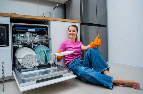 Young woman sitting on the floor near the dishwasher machine