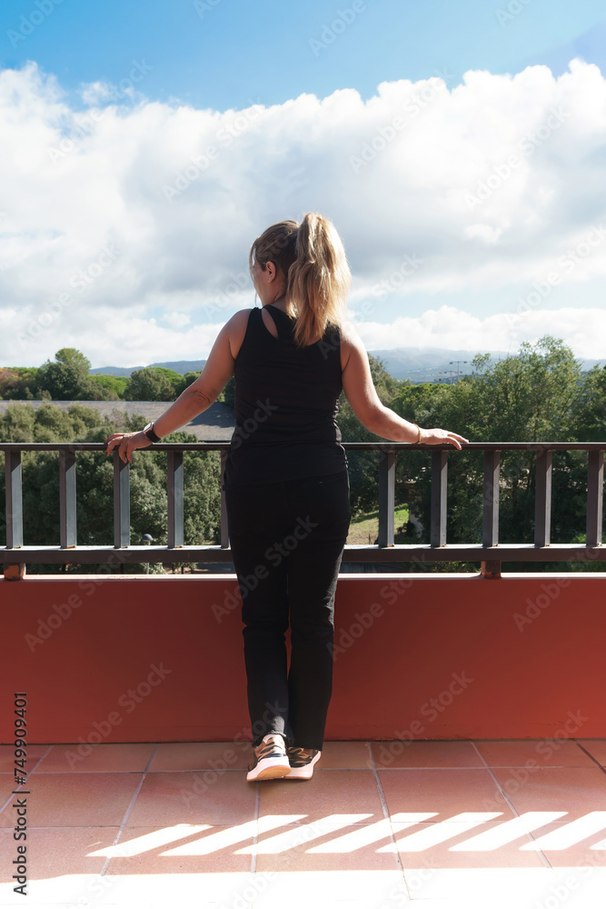 Rear view of a young girl with pony tail leaning out of a balcony looking at the landscape.Rear view of a young girl with pony tail leaning out of a hotel balcony looking at the landscape.