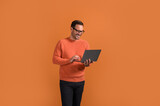 Smiling male manager checking e-mails over laptop while standing confidently on orange background