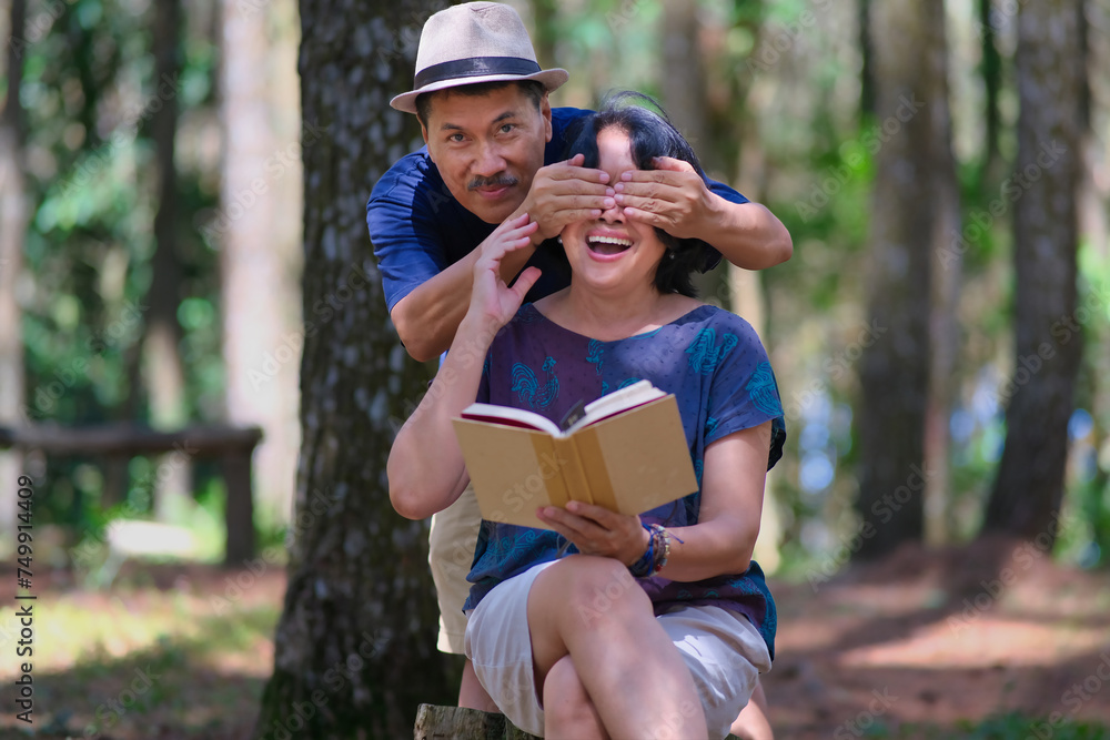 Fototapeta premium Man covering a woman's eyes with both hands from the back, while she was reading a book