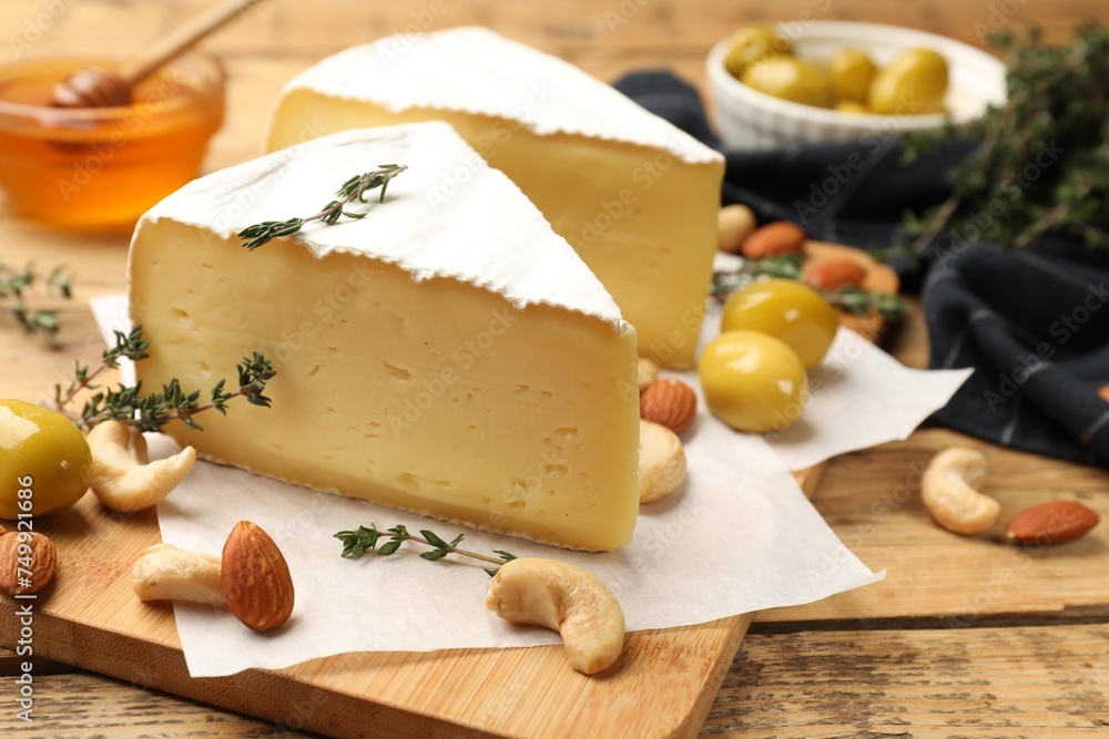 Tasty Camembert cheese with thyme, olives and nuts on wooden table, closeup Tasty Camembert cheese with thyme, olives and nuts on wooden table, closeup