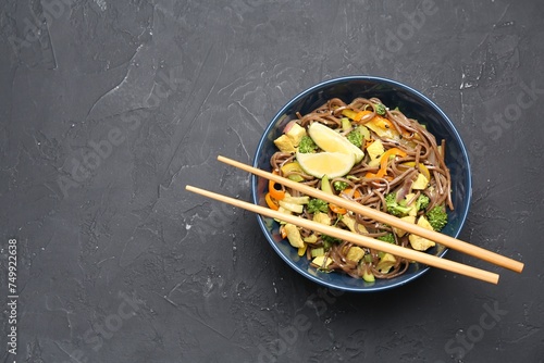 Stir-fry. Delicious cooked noodles with chicken and vegetables in bowl served on gray textured table, top view. Space for text