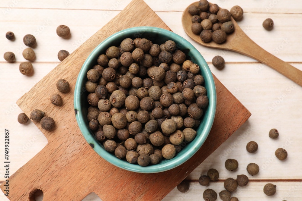 Dry allspice berries (Jamaica pepper) in bowl and spoon on light wooden table, flat lay Dry allspice berries (Jamaica pepper) in bowl and spoon on light wooden table, flat lay
