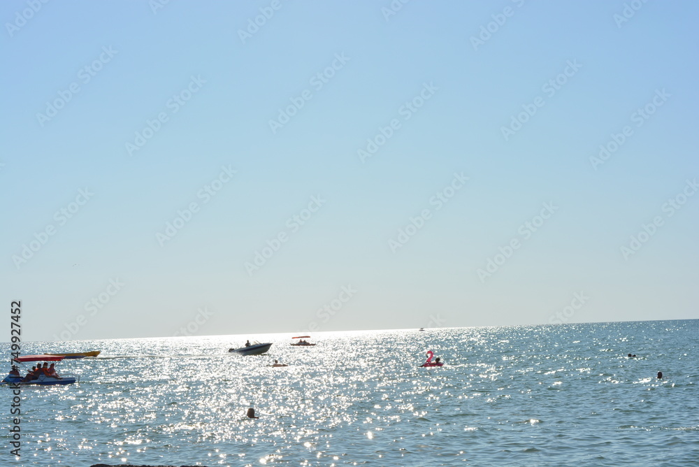 Beautiful border between the blue sky and the black sea with small waves and fine golden and bright reflections of the sun on the water.