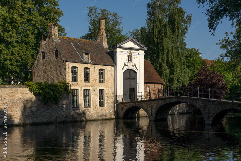 Begijnhof bridge in the old town of the beautiful city of Bruges in Belgium, with its historic facades reflected on the canal in a sunny day.