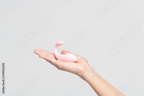 Close-up view of adult caucasian woman holding in her hand small pink vibrator against gray background. Soft focus. Adult sex toys theme.