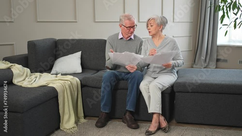 Sad tired disappointed middle aged senior couple sit with paper document. Unhappy older mature man woman reading paper bill managing bank finances calculating taxes planning loan debt pension payment