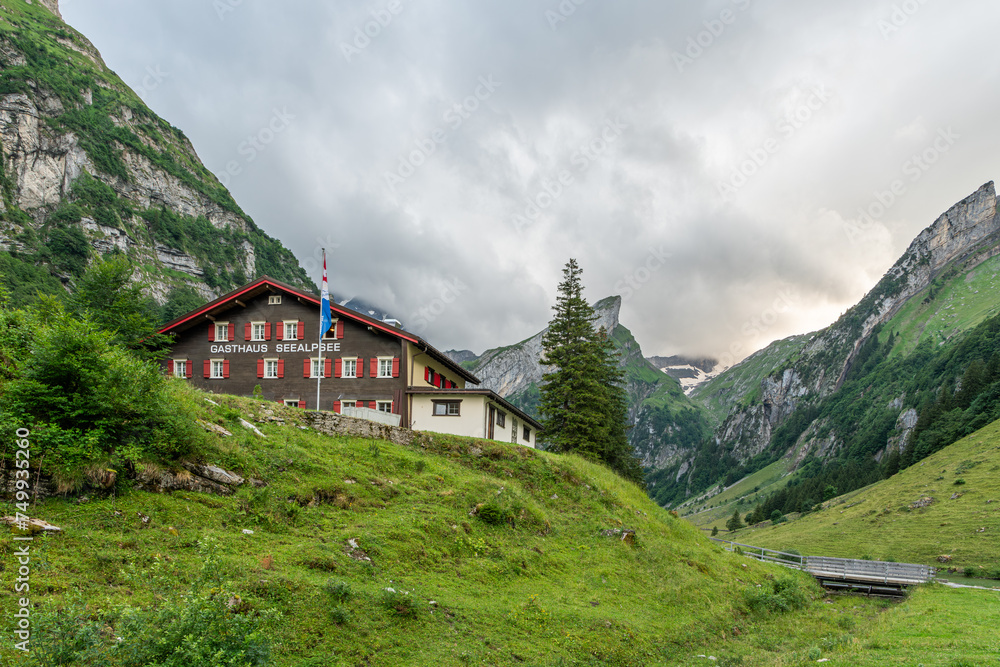 Evening view of the Swiss mountain hut at the Seealpsee lake in the Appenzeller Alps. Mountain refuge surrounded by steep Alpine mountains and pine trees in Switzerland. Beautiful hiking spot.