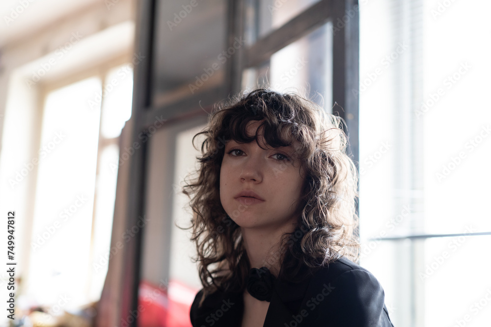portrait of a young beautiful woman with curly hair standing near the window in black clothes portrait of a young beautiful woman with curly hair standing near the window in black clothes