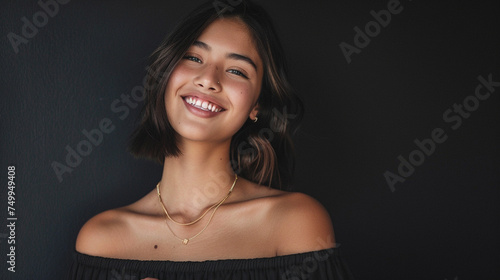 Against a matte black background, a chic young woman with a sleek lob haircut, wearing an off-the-shoulder shirt and delicate gold jewelry, beams with confidence photo