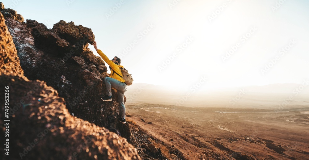 Male hiker climbing the mountain - Strong hiker standing on the top of the cliff enjoying sunset view - Extreme sport life style concept - obrazy, fototapety, plakaty 