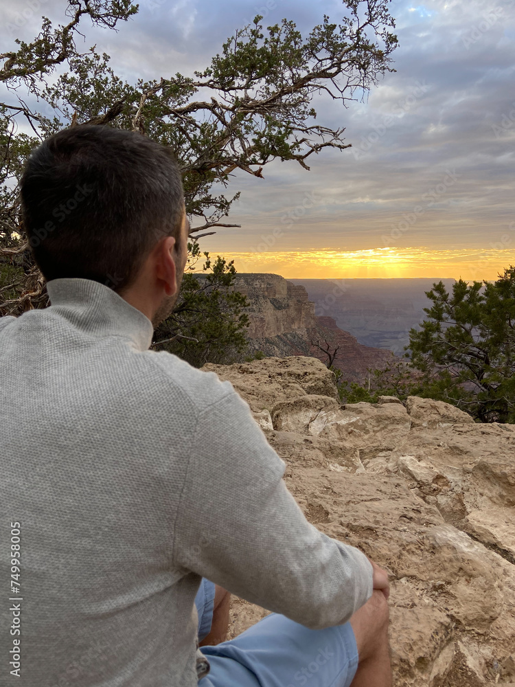 A tourist man enjoying the view of the South Rim of the Grand Canyon National Park at sunset.