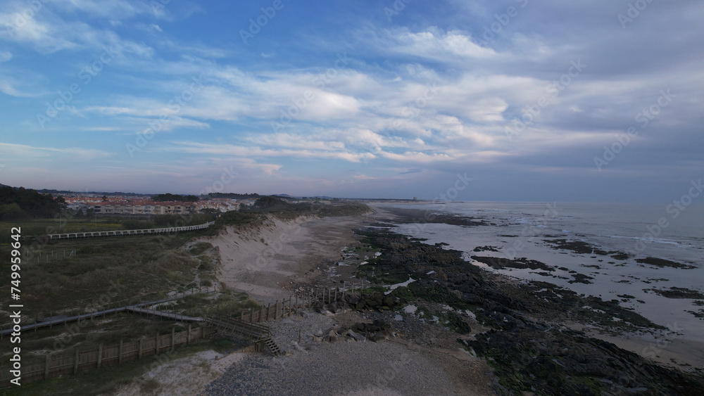 Sea, beach boulders, pebble shore, and waves at sunset. Sea waves breaking on rocks. Beach with sand dunes and dusk sky in Rio de Moinhos, Esposende, Portugal.