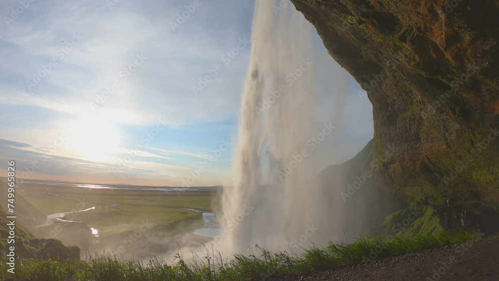 The Seljalandsfoss waterfall on the south coast of Iceland bathed in the otherworldly light of the midnight sun. The waterfall drops 60 meters and is part of the Seljalands River.