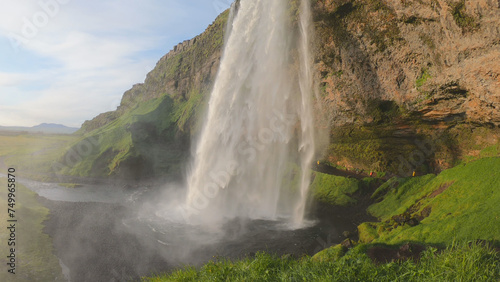 The Seljalandsfoss waterfall on the south coast of Iceland bathed in the otherworldly light of the midnight sun. The waterfall drops 60 meters and is part of the Seljalands River.