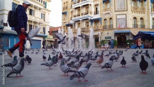 A man with a backpack walks against the backdrop of the Old Medina. There are many birds in the foreground. Slow motion.