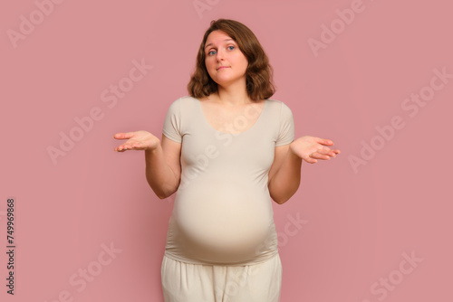 A doubting pregnant woman on a studio pink background. Pregnancy in a thoughtful woman with a belly, copy space