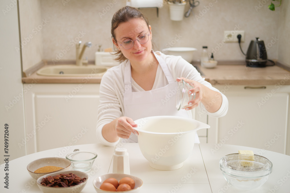 Young woman is making cookies in the kitchen at home. She is wearing apron and glasses. Process of cooking pecan pie in home kitchen for American Thanksgiving Day. Young woman is making cookies in the kitchen at home. She is wearing apron and glasses. Process of cooking pecan pie in home kitchen for American Thanksgiving Day.