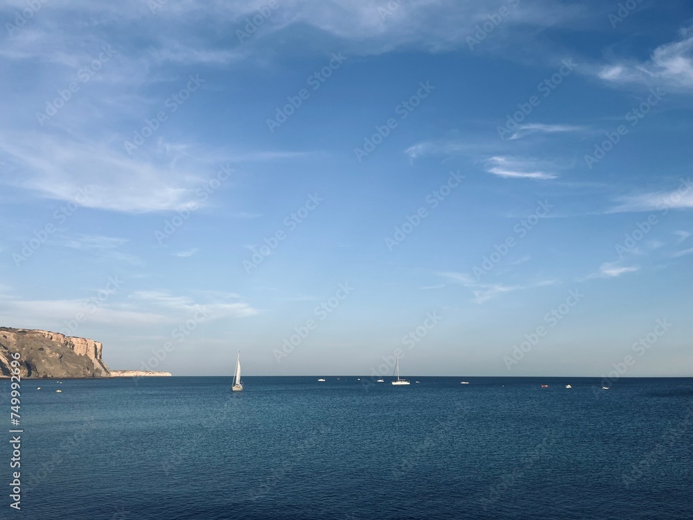 Fototapeta premium White sail boats at the ocean, blue ocean horizon, rocky coast