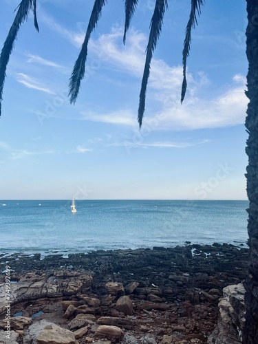 White sail boats at the ocean, blue ocean horizon, rocky coast