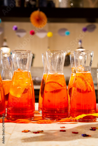 Vivid Aperol Spritz pitchers with orange slices on party table with festive background
