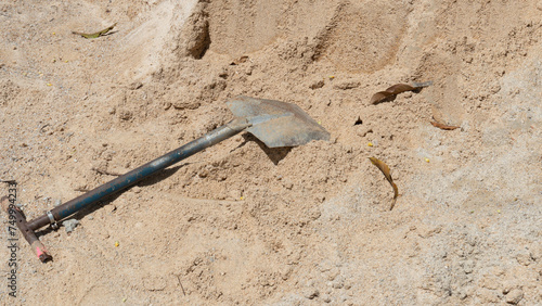 Construction background. Steel of shovel is propped up on a pile of sand. Outdoors in the sun.