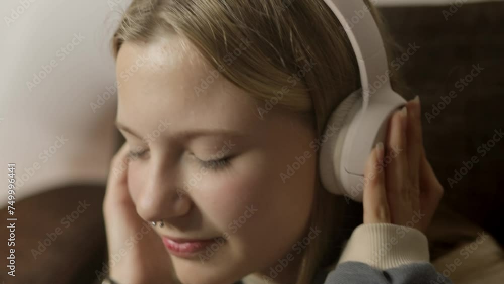 Seated on the couch, a hipster girl with a nose piercing enjoys music through her headphones, expressing her individuality in style and taste. Seated on the couch, a hipster girl with a nose piercing enjoys music through her headphones, expressing her individuality in style and taste.
