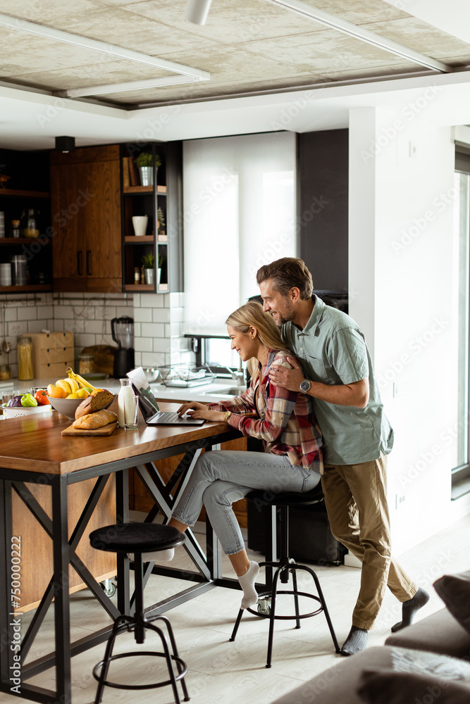 Cheerful couple enjoys a light-hearted moment in their sunny kitchen, working on laptop surrounded by a healthy breakfast Cheerful couple enjoys a light-hearted moment in their sunny kitchen, working on laptop surrounded by a healthy breakfast