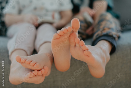 Big brother and little sister holding bare feet close up to camera . Blurred face on background 