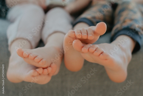 Big brother and little sister holding bare feet close up to camera . Blurred face on background 