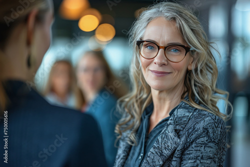 middle-aged businesswoman with specs shaking hands with other women in an office space background.