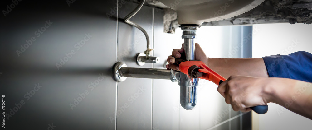 Plumber uses wrench to repair water pipe under sink There is maintenance to fix the water leak in the bathroom.with red wrench, plumbing install concept. Plumber uses wrench to repair water pipe under sink There is maintenance to fix the water leak in the bathroom.with red wrench, plumbing install concept.