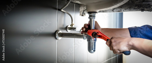 Plumber uses wrench to repair water pipe under sink There is maintenance to fix the water leak in the bathroom.with red wrench, plumbing install concept.