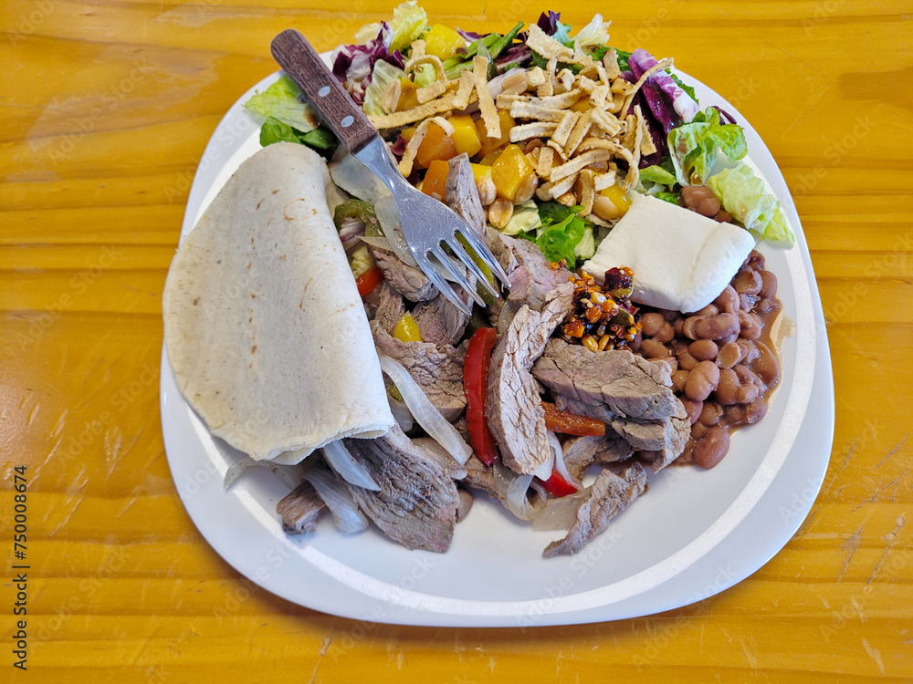 A filling Mexican fajita plate with tender sliced beef, pinto beans, fresh salad, and a soft tortilla, ready to satisfy any appetite