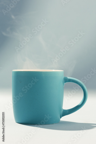 Morning hot steaming blue cup of coffee on blue background with sunlight