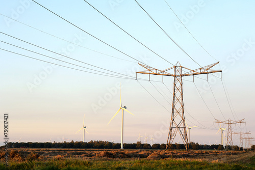 High voltage pole with power transmission  lines crossing  wind turbine  field in the background.