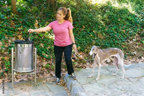 Canvas Print Young Spanish woman with a greyhound dog throwing a bag of her dog's feces into a garbage can