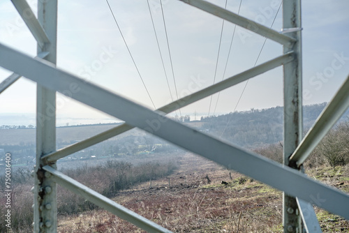 Looking through metal frame of electric transmission tower at mountain valley with cut forest for cable passage. High-voltage electricity pylons on a sunny day in rural countryside highland landscape. photo