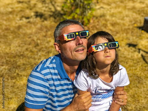 Father and daughter, family viewing solar eclipse with special glasses in a park
