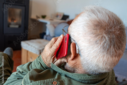 Detail of unrecognisable old man with his back turned talking on the telephone, hearing aid in his ear. Dressed in green shirt, grey hair