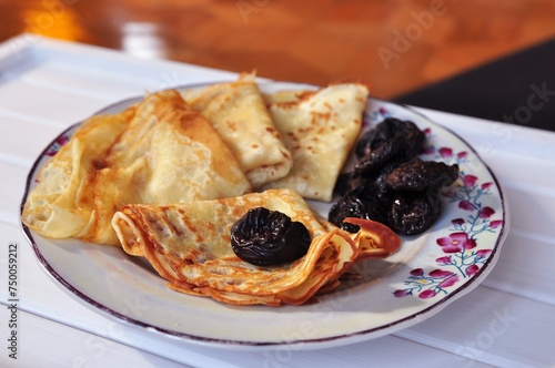Delicious pancakes dessert for breakfast. Sweet pancakes with prunes on the plate with flowers on white table. Tasty food of Ukrainian cuisine. 