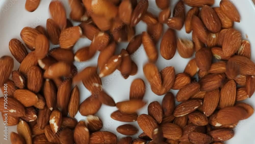 Roasted nuts almonds pouring into plate slow motion top view. Roasted nuts almonds pouring into plate slow motion top view.