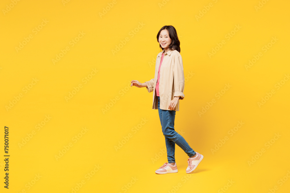 Full body side profile view young woman of Asian ethnicity she wearing pink t-shirt beige shirt pastel casual clothes walk go isolated on plain yellow background studio portrait. Lifestyle portrait. Full body side profile view young woman of Asian ethnicity she wearing pink t-shirt beige shirt pastel casual clothes walk go isolated on plain yellow background studio portrait. Lifestyle portrait.