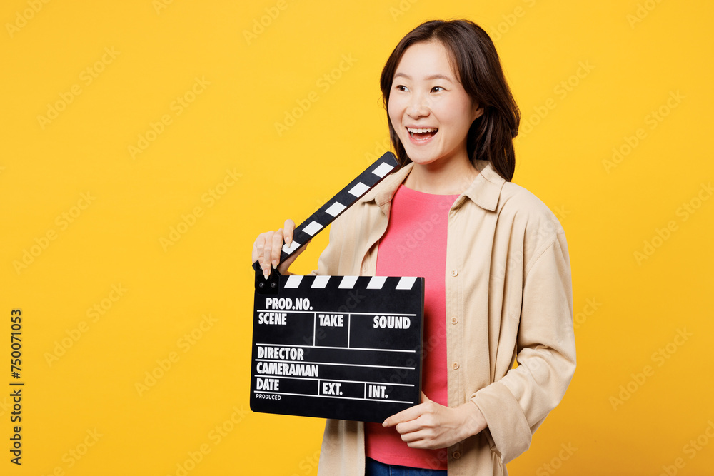 Young woman of Asian ethnicity wear pink t-shirt beige shirt pastel casual clothes hold in hand classic black film making clapperboard isolated on plain yellow background studio. Lifestyle portrait.